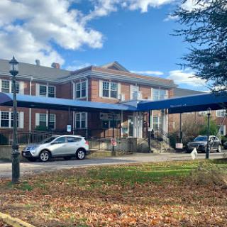 A view of a brick building with a blue awning and parked cars under a partly cloudy sky.