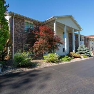 Front view of a residential house with brick exterior, surrounded by landscaped greenery and a paved driveway.