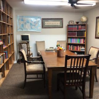 A cozy office with a large table surrounded by chairs and bookshelves filled with books.