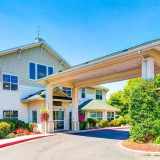 A modern building entrance with an extended awning and landscaped surroundings on a bright, sunny day.
