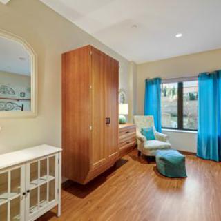 A cozy bedroom with wooden flooring, featuring blue curtains and an armchair by the window.