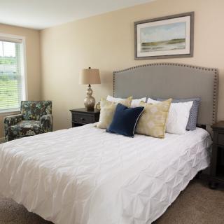 A cozy bedroom with a neatly made bed, decorative pillows, and a landscape painting on the wall.