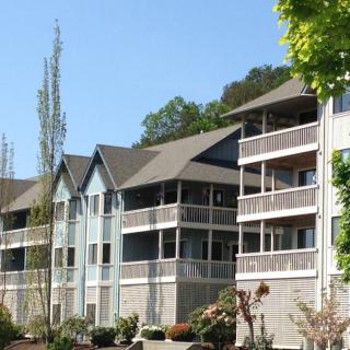 A modern apartment building with multiple balconies set against a clear blue sky, surrounded by trees.