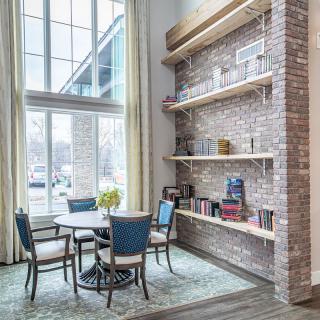 A cozy modern living space with a brick wall and large windows, featuring a round table with chairs and built-in bookshelves.