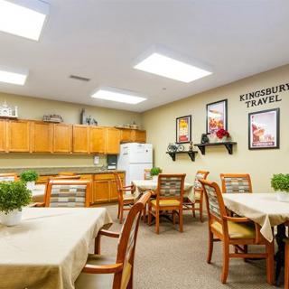 A well-lit dining area with wooden tables and chairs, adorned with plants and decorative artwork on the walls.