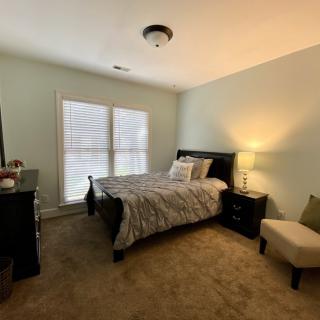 A cozy bedroom with a bed, dresser, chair, and lamp.