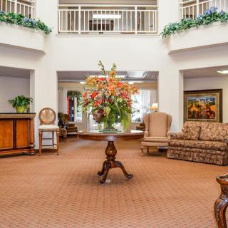 A luxurious hotel lobby featuring elegant furniture and a large floral arrangement on a central table.