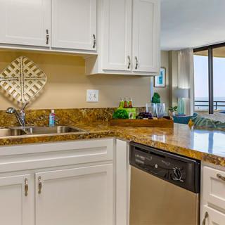 A modern kitchen featuring white cabinets and a granite countertop, complete with a sink and dishwasher.