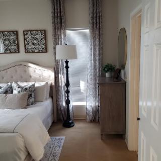 A cozy bedroom with elegant decor, featuring a bed, dresser, and floor lamp.
