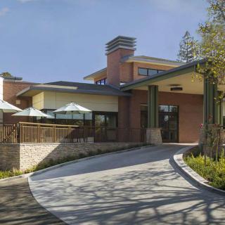 A modern building with a driveway leading to its entrance, featuring a blend of materials and outdoor seating.