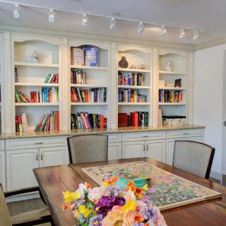 A cozy dining room featuring a wooden table with vibrant flowers and a large bookshelf filled with various books.
