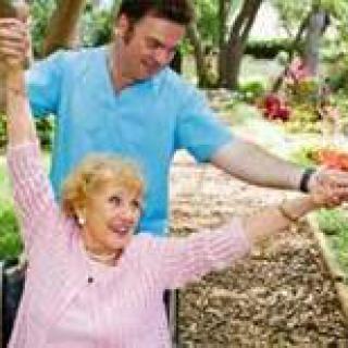 A caregiver assists a joyful senior woman in a wheelchair, enjoying the outdoors in a garden setting.