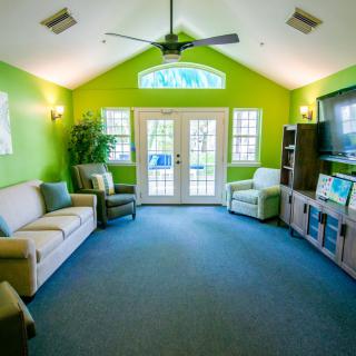 A bright and colorful living room with green walls, featuring comfortable seating and a television.