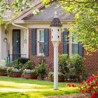 A charming brick house with a well-maintained garden and birdhouse in the front yard.