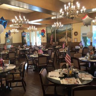 A decorated dining area with balloons and flags, featuring multiple tables and elegant chandeliers.