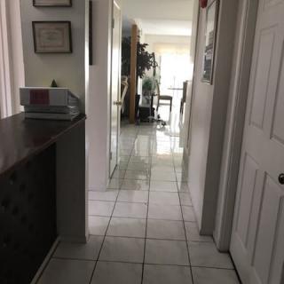 A view down a tiled hallway in a home, leading to a bright room with furniture and decor.