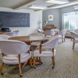 A well-lit conference room with round tables and upholstered chairs, featuring a carpeted floor and large windows for natural light.
