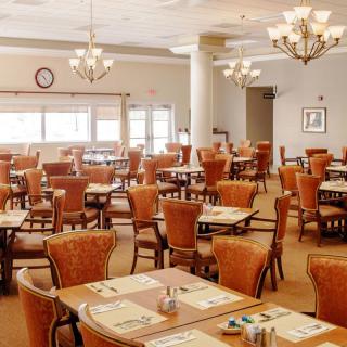 An elegant dining room with neatly arranged tables and chairs, illuminated by chandeliers.