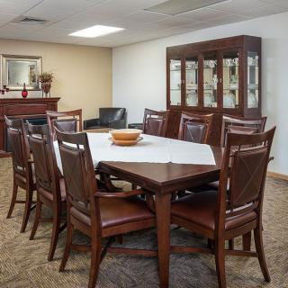 A formal dining room with a large wooden table, surrounded by chairs and a cabinet in the background.