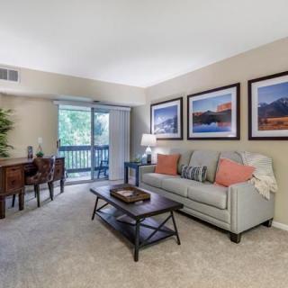 A cozy living room with a sofa, coffee table, and wall art, leading to a dining area and balcony.