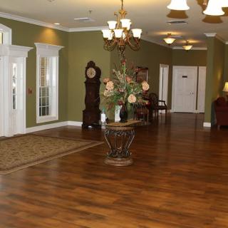 A traditional lobby with a grandfather clock, chandelier, and decorative flowers on a hardwood floor.