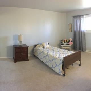 A minimalist bedroom featuring a single bed, nightstand with a lamp, and a chair by the window.