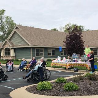 A group of elderly individuals in wheelchairs are enjoying a social gathering outside a care facility.