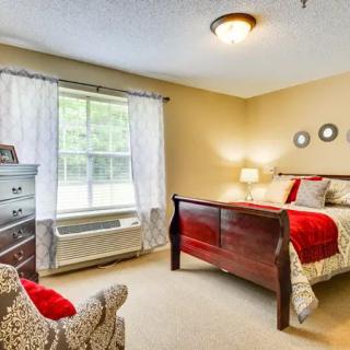 A cozy bedroom with a wooden bed, patterned bedding, and natural light from a large window.