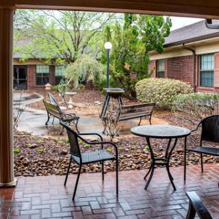 A serene courtyard featuring outdoor seating with benches and tables surrounded by lush greenery.