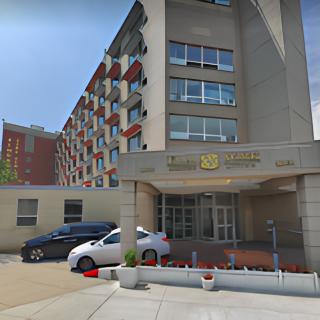 The entrance of a modern hotel building with parked cars in an urban setting.