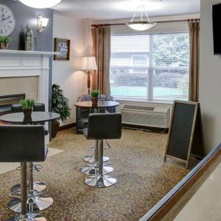 A cozy and modern seating area with tables, chairs, a fireplace, and natural light coming through a large window.