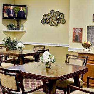 A well-decorated dining room with tables and chairs, featuring a television and floral arrangements.