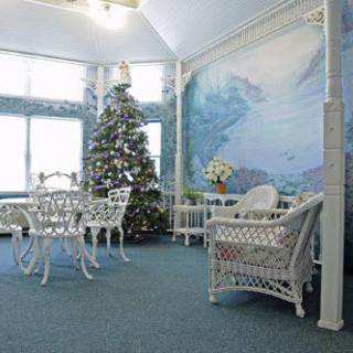 A cozy conservatory decorated for the holidays with a Christmas tree and wicker furniture.