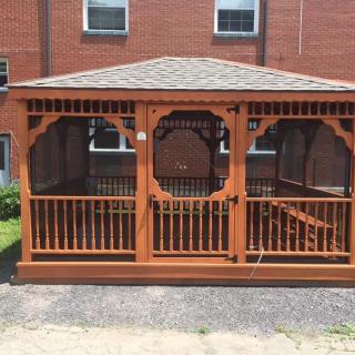 A wooden gazebo situated in front of a brick building.