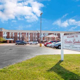 Exterior view of an apartment complex with a parking lot and sign on a sunny day.
