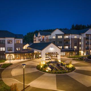 A well-lit hotel or residential building at night with a landscaped entrance.