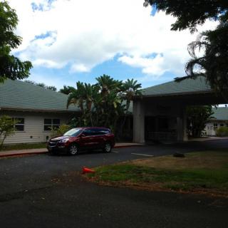 A car parked in front of a building surrounded by trees under a cloudy sky.