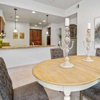 A modern dining area featuring a round wooden table with decorative candles, surrounded by upholstered chairs and illuminated by pendant lights.