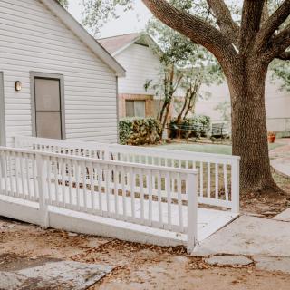 A white house with an accessibility ramp and a large tree in the yard.