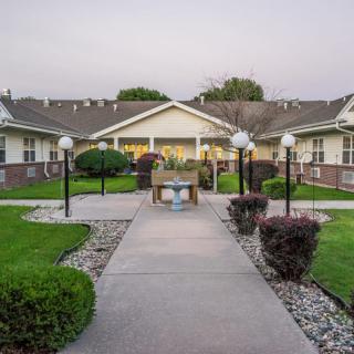 A well-maintained building exterior with a paved pathway, surrounded by lush greenery and outdoor lighting.