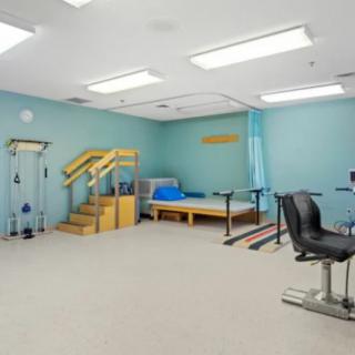 A physical therapy room equipped with exercise machines, parallel bars, and a staircase for rehabilitation exercises.