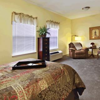 A cozy bedroom with a bed, armchair, and table, decorated in warm tones.
