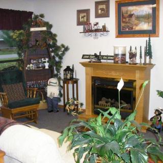A cozy living room with a fireplace and various decorative elements, including plants, wall art, and a rocking chair.