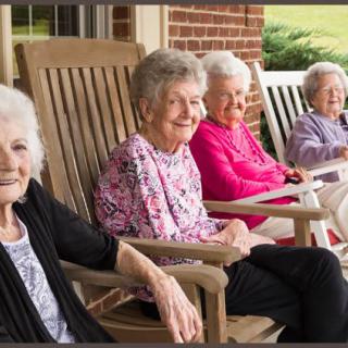 A group of elderly women sitting on rocking chairs on a porch, enjoying the outdoors.