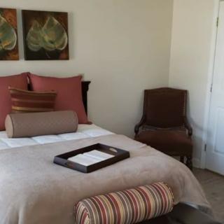 A cozy, well-decorated bedroom with artwork above the bed and a cushioned chair in the corner.
