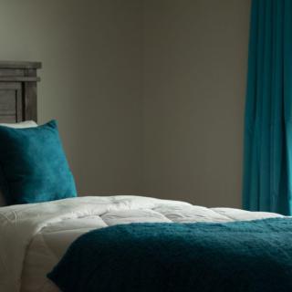 A cozy bedroom with a teal color scheme featuring a neatly made bed and matching curtains.