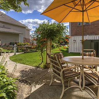 A sunny backyard with a patio table and umbrella, surrounded by a well-kept garden.