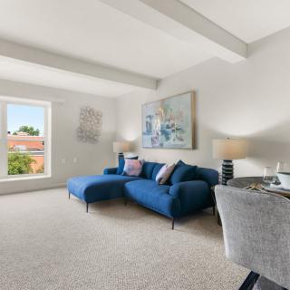 A bright and spacious living room with a blue sofa and modern decor, featuring large windows that allow natural light to fill the space.