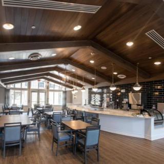 A modern restaurant interior featuring a dining area with a wooden ceiling and ample seating.