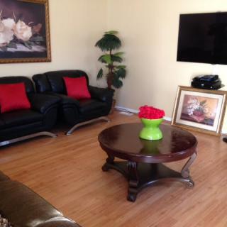 A cozy living room featuring a black sofa with red pillows, a wooden coffee table, wall-mounted TV, and decorative elements like paintings and plants.